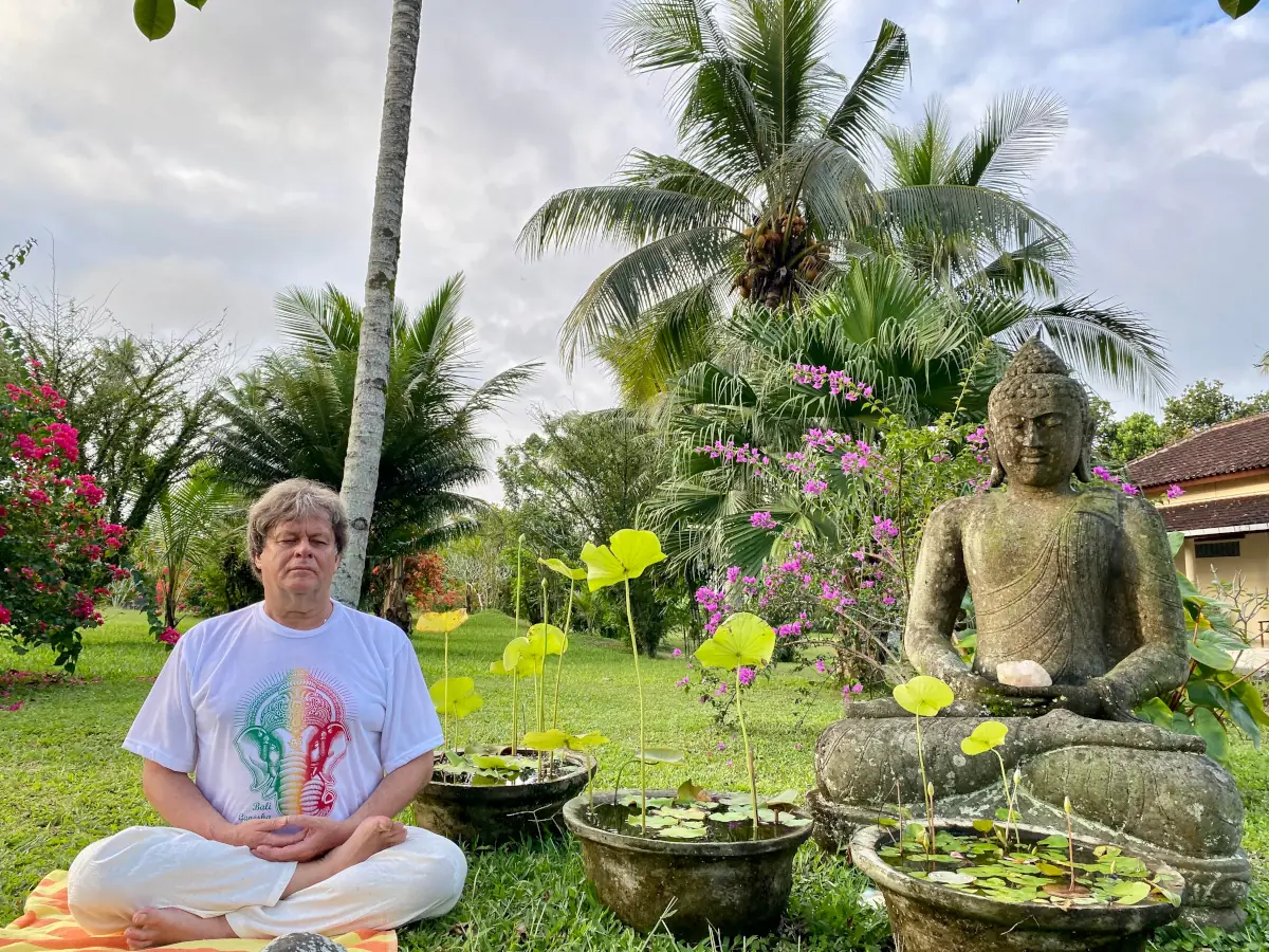 Yogadocent Berry mediteert naast een boeddhabeeld in een tuin op Bali